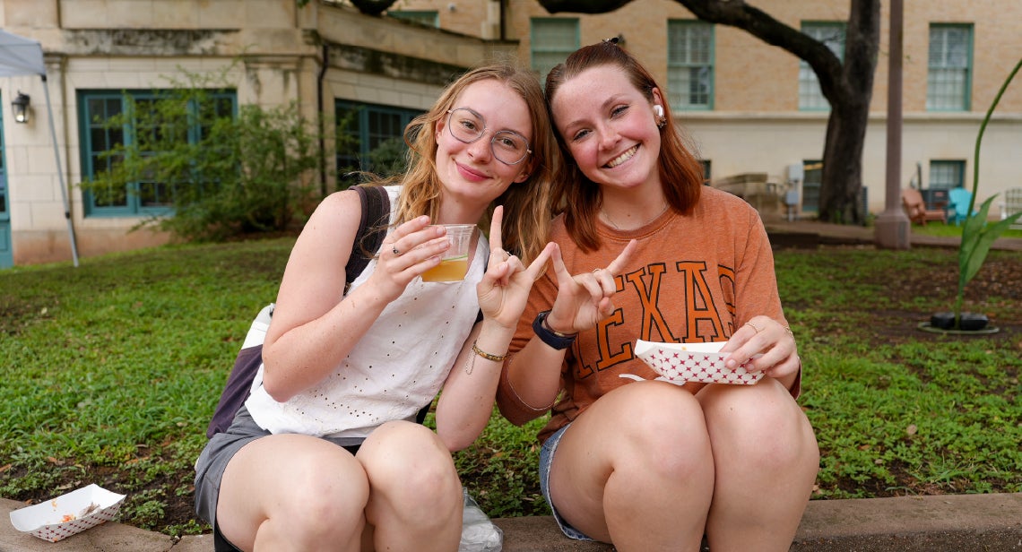 Two UT students holding up a Hook ‘em hand sign sitting in the Quad courtyard.