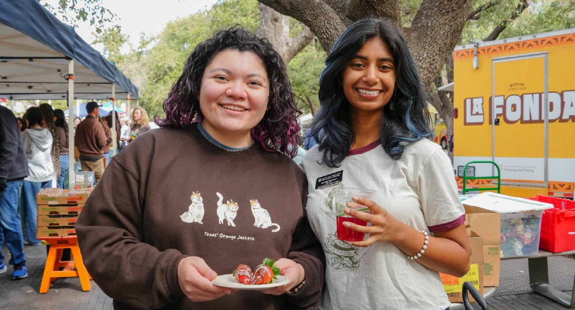 Two UT students smiling and holding refreshments at a UT Farm Stand market.