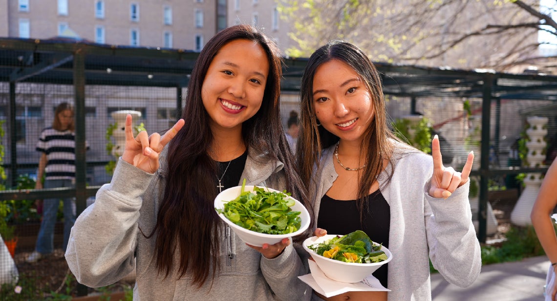 Two UT students holding a Hook ‘em hand sign and salads at the Pick Local event at Jester Gardens.