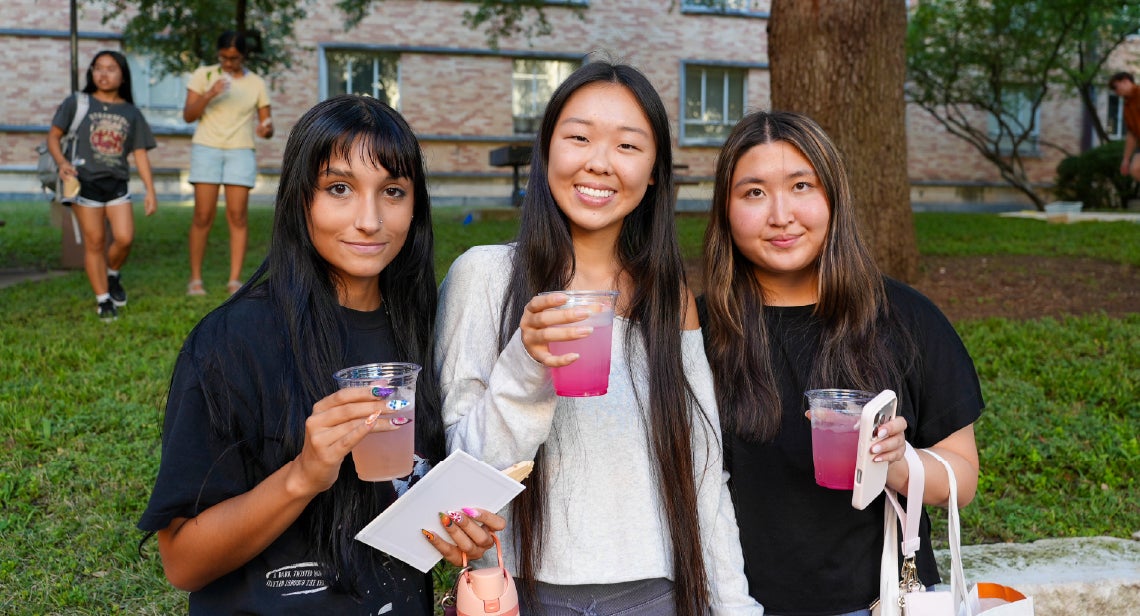 Three UT students smiling while holding drinks at the Quad Courtyard.