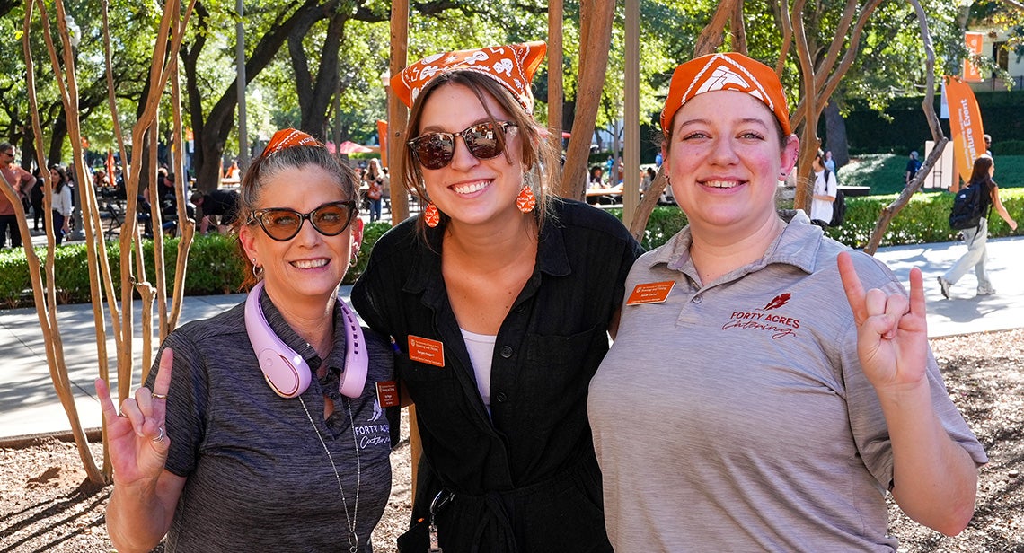 Three UHD staff members pose together while making the Hook ‘em hand sign on Speedway