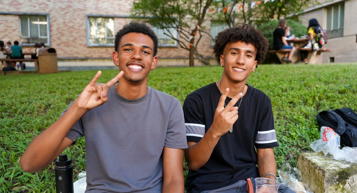 Two UT students smiling while holding up a hook ‘em hand sign and a peace sign.