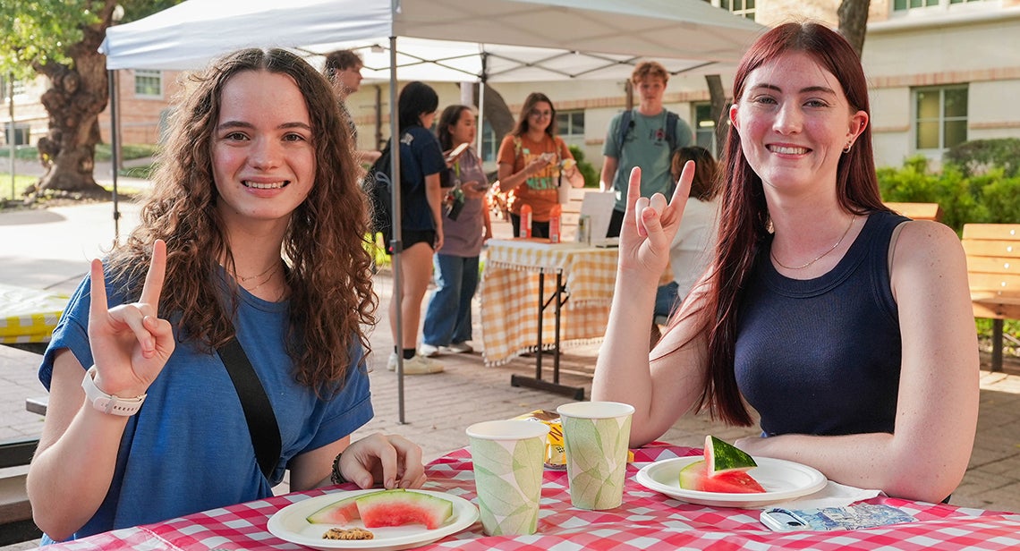 Two students posing with a Hook ‘em hand sign