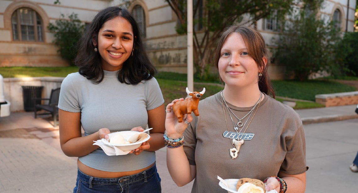 Two UT students smiling while holding a longhorn stress reliever outside of San Jacinto hall.