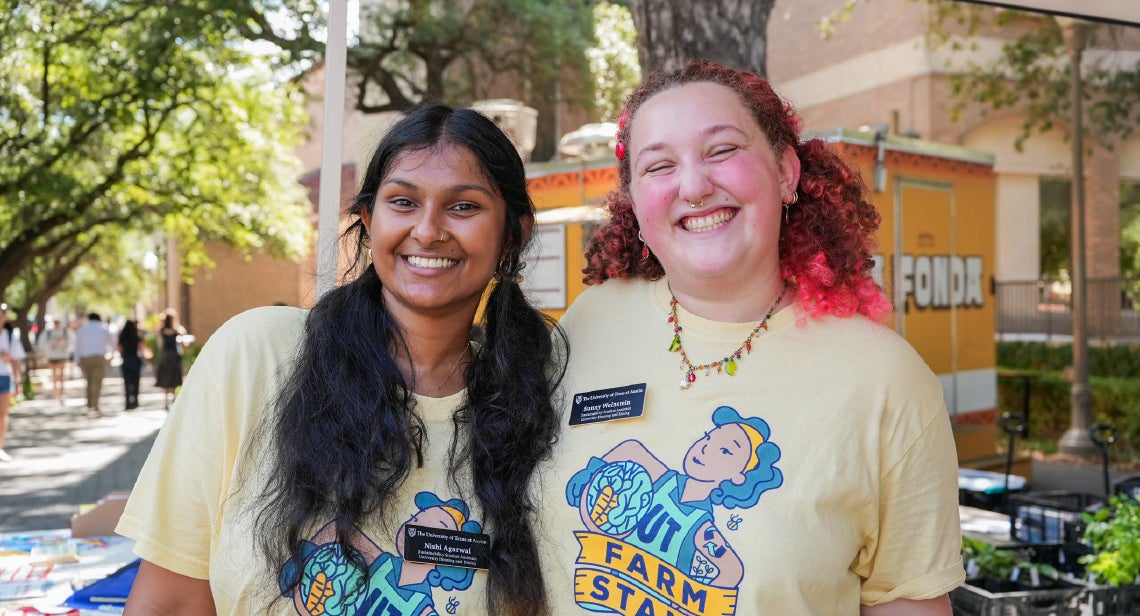 Two UT Farm Stand student volunteers smiling in front of Jester West hall.