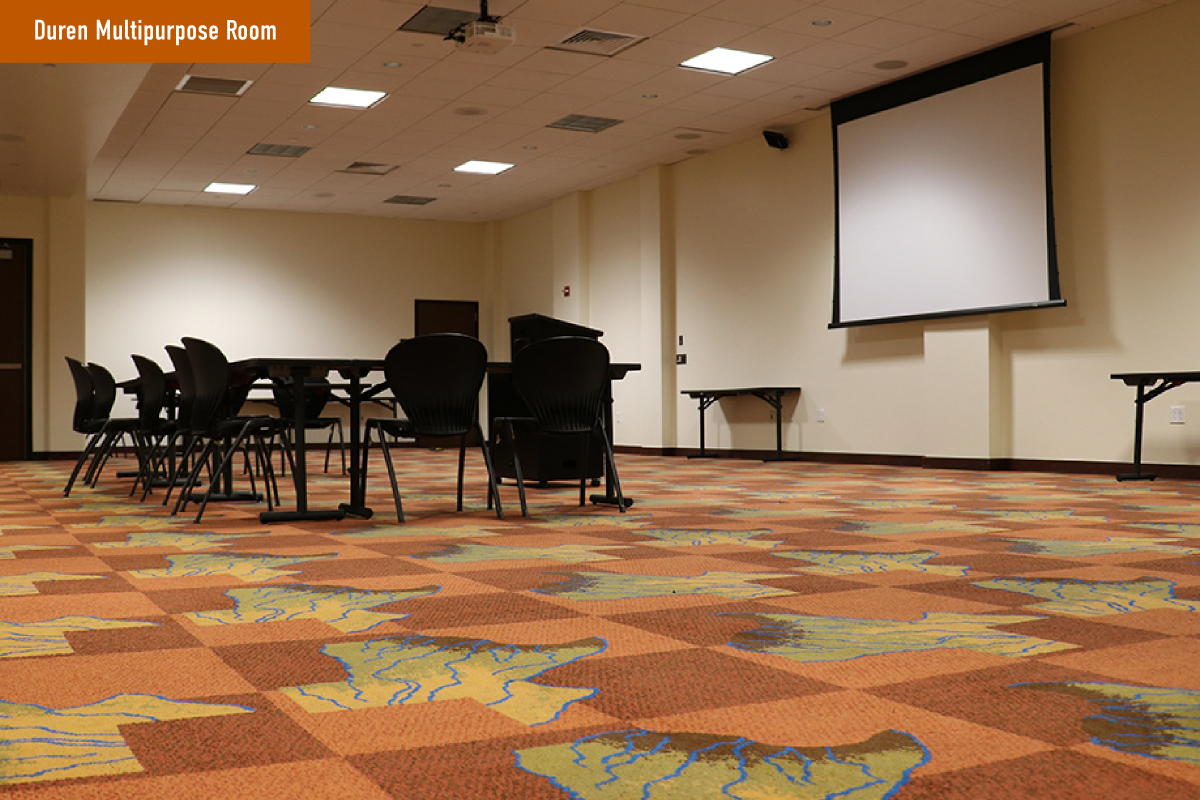 A view of a table and chairs, along with a projector screen in the Duren Multipurpose Room.