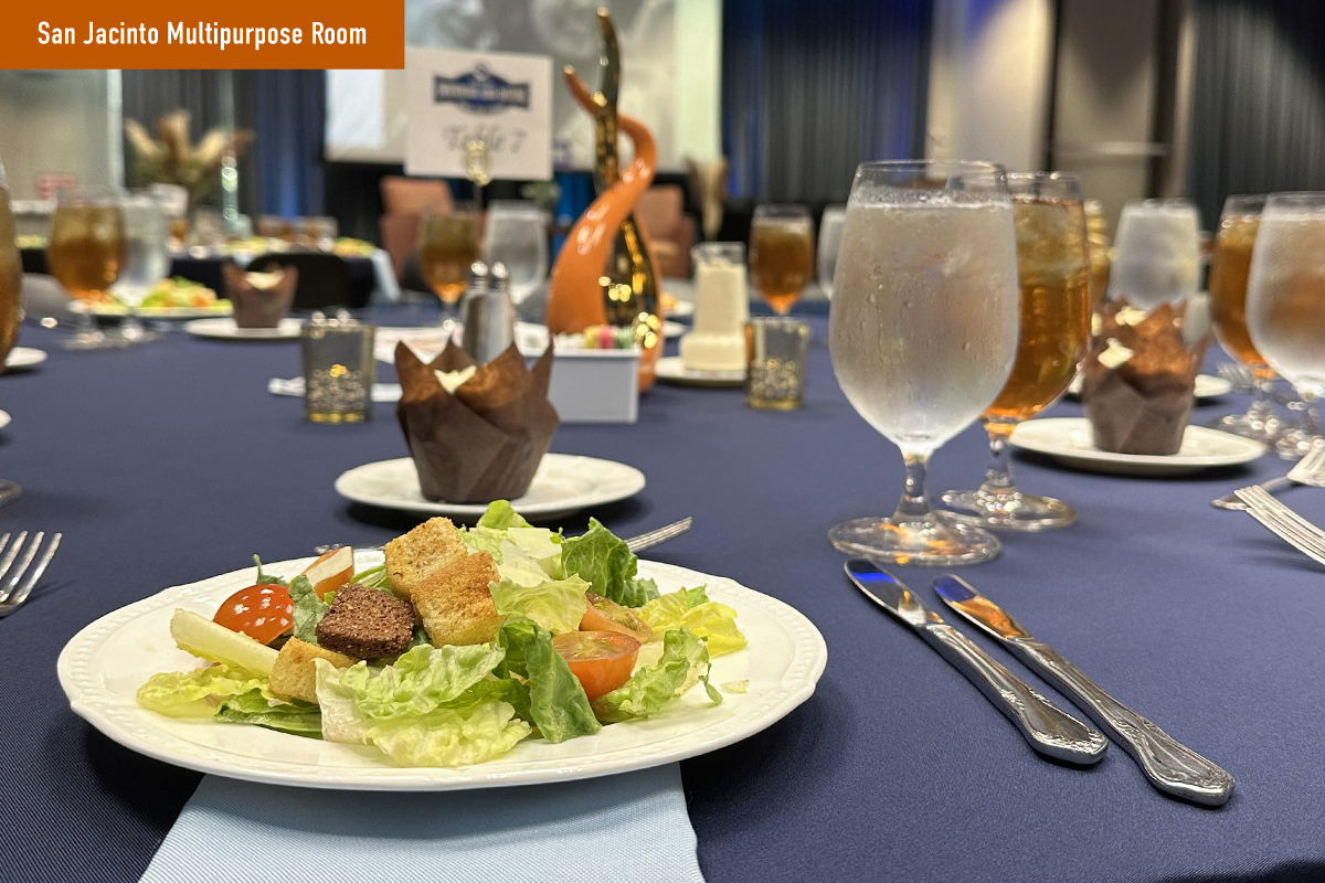 A close-up view of a salad, silverware, and glasses filled with water and iced tea at a private event catered by Forty Acres Catering.