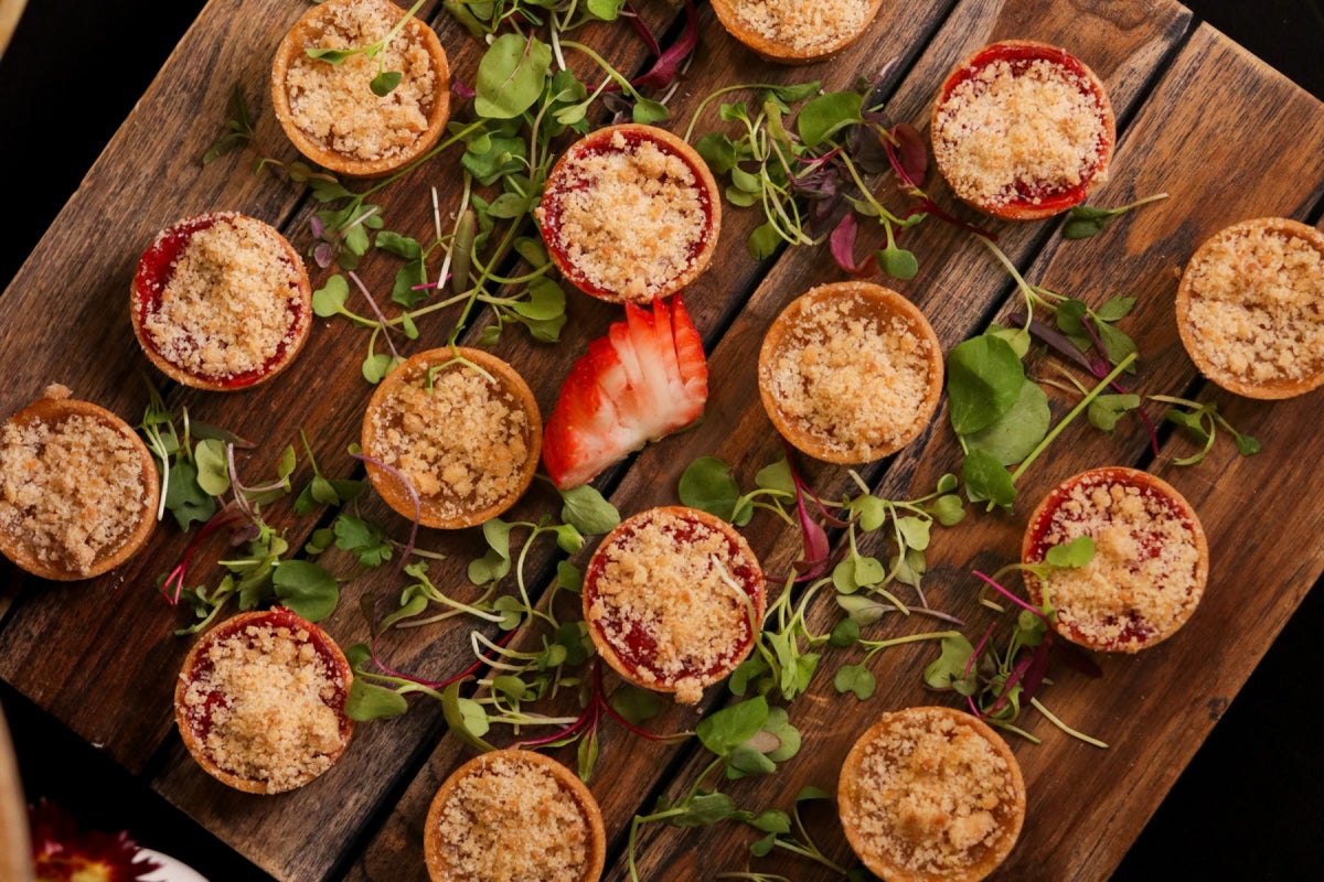 Mini fruit tarts served on a wooden board with green garnishes