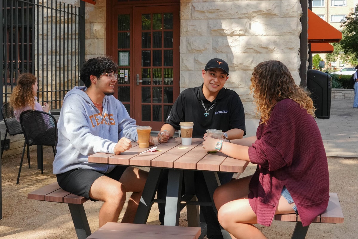 A group of UT students and a student staff member converse outside Littlefield Patio Cafe.