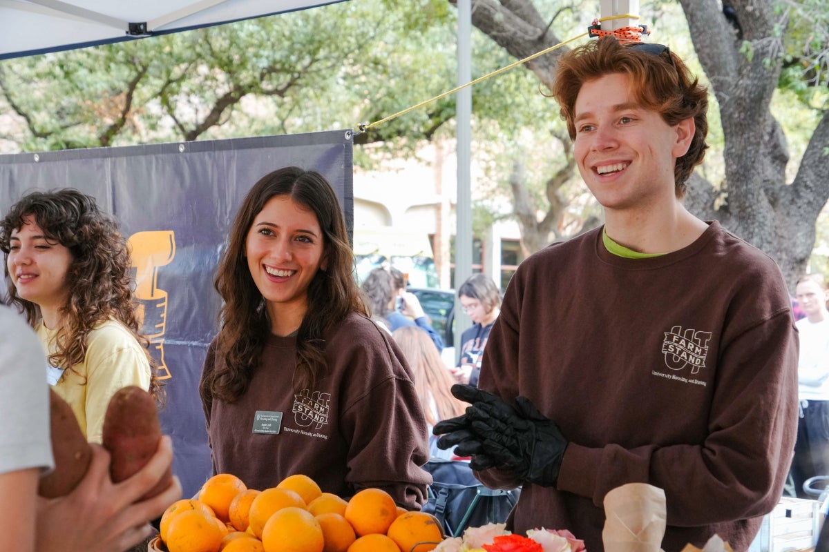 Two UT students smile as they hand over produce to a student at the UT Farm Stand