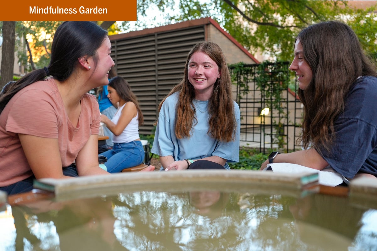 Three UT students talk and smile together at the Mindfulness Garden