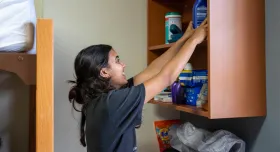 A student in a residence hall room at UT reaches for supplies on a shelf.