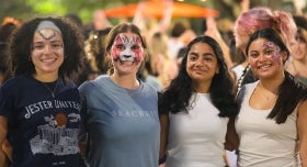 Four students with painted face-masks pose together and smile