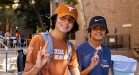 A UT Student and family member posing with a hook 'em hand sign outside of Jester Residence Hall