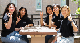 A group of UT resident assistants sit at a table at Jester Plaza while making the Hook ‘em hand sign.