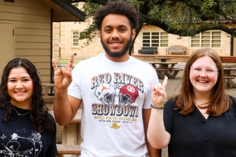 Three students smiling outside while posing with University of Texas hand symbol.