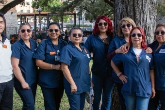 Eight UHD staff members in work uniforms at an employee event in the Honors Quad courtyard.