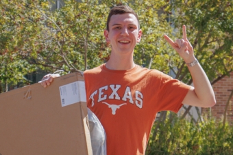 A student poses outside with a package during spring checkout from his hall