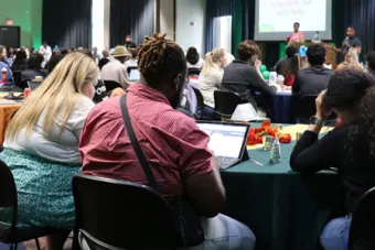 Event guests sit around tables while listening to presenters in San Jacinto Multipurpose Room.