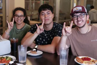 Three UT students pose together and make the Hook 'Em hand sign at J2 Dining.
