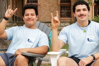 Two Resident Assistants make the Hook ‘Em hand sign in front of Littlefield Hall.