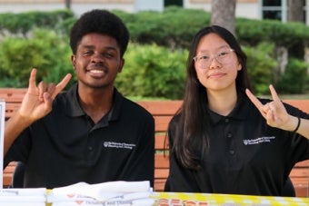 Two UT student staff members pose together on a bench while making the Hook 'em hand sign