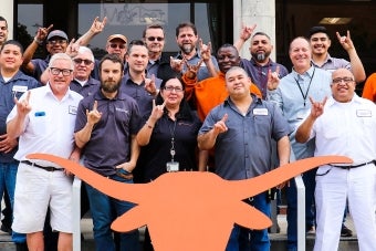A group of UT staff members pose together while making the Hook ‘em hand sign behind a Longhorn silhouette