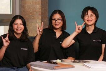 Five UT resident assistants pose while making the Hook ‘em hand sign in the Jester Fireplace Lounge