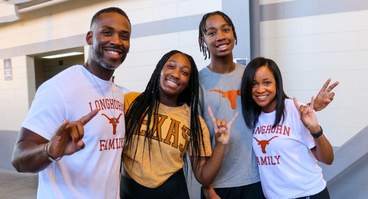 A family of four pose at Mooov-In. Three of the family members pose with hook em hands and one poses with a peace sign. 