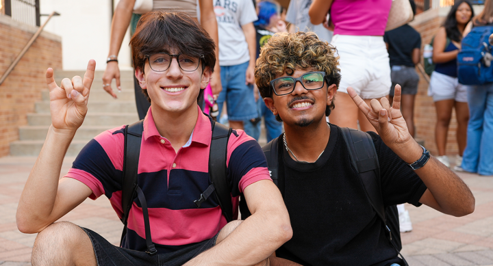 Two UT students sitting on stairs, posing with a Hook ’em hand sign